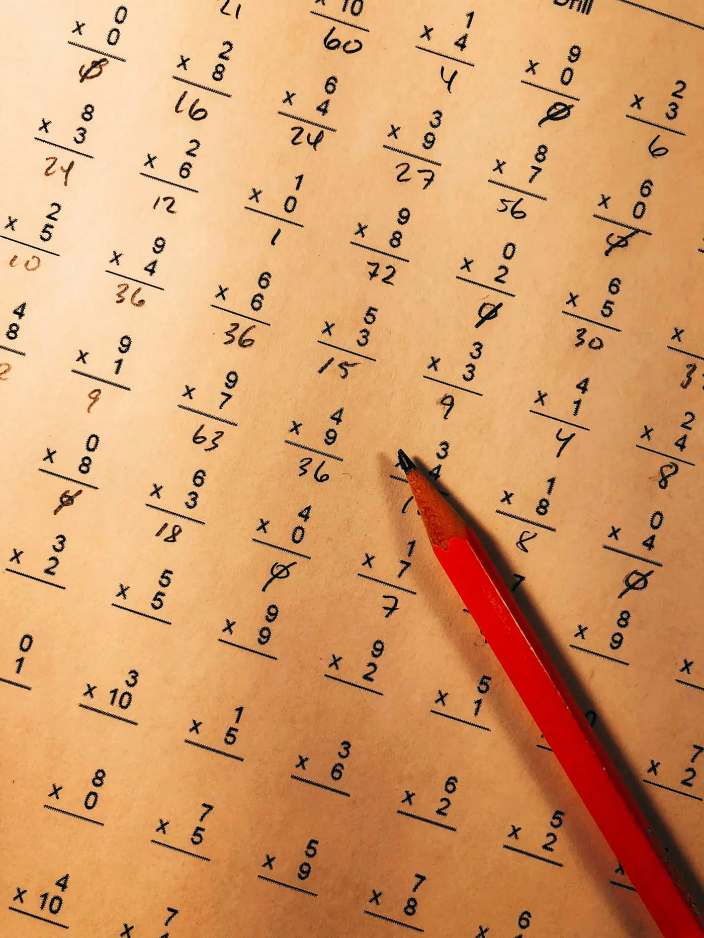 A red pencil resting on a page of handwritten arithmetic