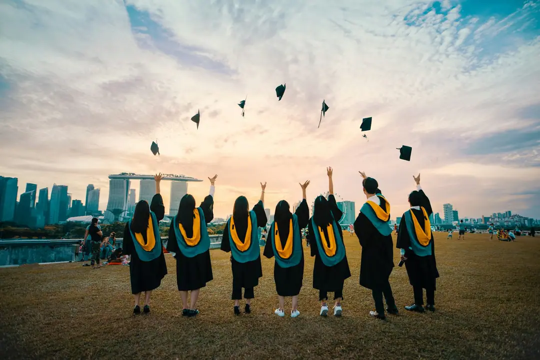 A row of graduates throw their mortarboards into the sky at sunset