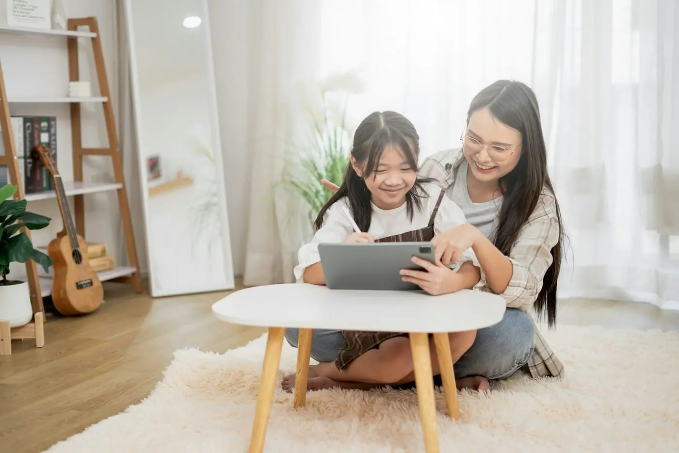 A parent and child sit on the floor of a living room looking at a tablet