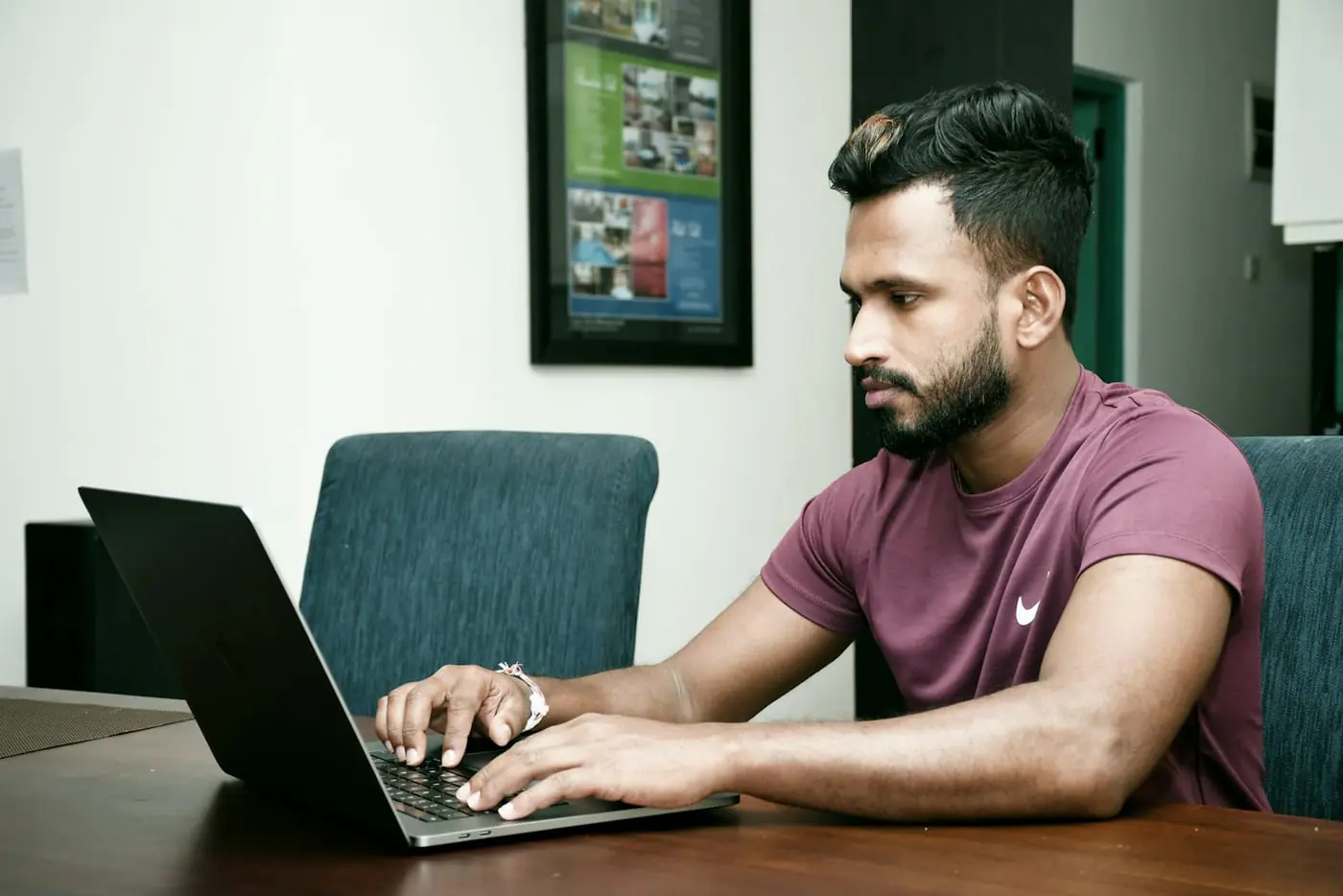 A university-age student works on a laptop at a dining table at home