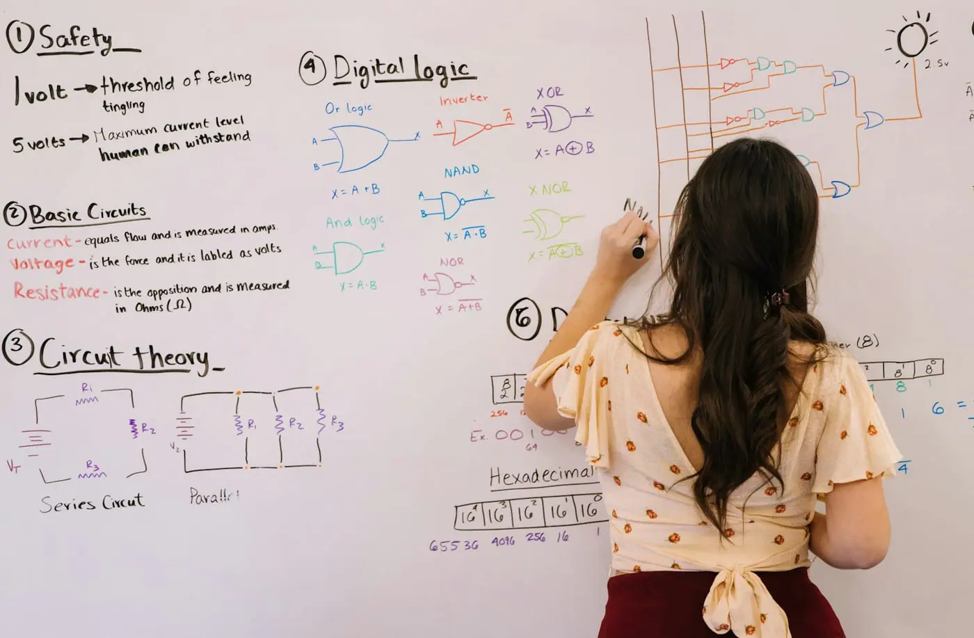 A teacher writes circuit theory and logic notes on a whiteboard