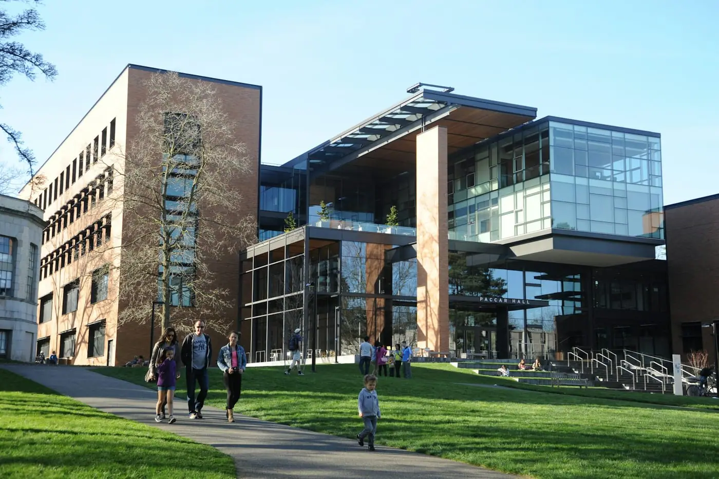 Students walk across a lawn in front of a modern university building